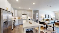 Located at 6705 Oak Grove Pkwy N in Brooklyn Park, MN, this 2-bedroom, 2-bathroom residence offers a thoughtfully designed single-floor layout with an open-concept living area that flows seamlessly from the kitchen through the dining space and into the living room. The kitchen is a standout feature, showcasing white shaker cabinetry with gold hardware, stainless steel appliances, a subway tile backsplash, and a center island with bar seating — all set atop durable wood-look flooring. The bright living room benefits from expansive windows that invite abundant natural light and provide outdoor views, with direct access to a private balcony. The generously sized primary bedroom features plush carpeting and connects to a well-appointed en-suite bathroom with a white vanity, gold fixtures, and a glass-enclosed shower. The second bedroom is equally comfortable with its own closet and convenient access to the second full bathroom, which mirrors the same refined finishes. Four closets throughout the residence provide ample storage. An in-unit laundry area adds everyday convenience. The overall aesthetic is clean and contemporary, with neutral tones and modern finishes creating a cohesive, welcoming ambiance throughout.