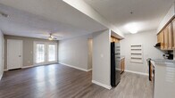 This well-appointed 3-bedroom, 2-bathroom single-floor residence at 6355 Oakley Rd in Union City, GA offers a comfortable and functional layout across a generous floor plan. The open living area is bright and welcoming, featuring durable wood-look flooring, neutral warm-gray walls, a textured ceiling, and a ceiling fan that runs throughout the main living spaces. French doors in the living room invite natural light and provide access to a private balcony overlooking a tree-lined exterior, adding a touch of greenery to everyday living. The galley-style kitchen is efficiently designed with warm wood cabinetry, light countertops, built-in shelving, and black appliances including a refrigerator, range, and dishwasher. Each of the three bedrooms offers ample space, ceiling fans, and easy access to the hallway. The spacious primary bedroom includes a dedicated walk-in closet with built-in shelving. Both bathrooms are finished with wood-look flooring, warm wood vanities, and light countertops. One bathroom features a soaking tub, while the other includes a vanity with a large mirror. A hallway connects all rooms cohesively, completing this practical and comfortable home.