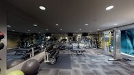 Located at 33 San Pablo Ave in San Rafael, California, this fitness center offers a comprehensive workout environment designed to support a wide range of exercise routines. The space is thoughtfully laid out across a single floor, with patterned carpet tile flooring throughout that defines different workout zones while providing cushioning underfoot.

The cardio section is well-stocked with treadmills, elliptical trainers, stationary bikes — including a Tour de France-branded cycling bike — and stair climbers, all positioned in front of wall-mounted flat-screen televisions for an engaging workout experience. Full-length mirrors line one wall, enhancing the sense of space and allowing exercisers to monitor their form.

The strength training area features a dumbbell rack with a broad range of weights, a weight bench, a cable machine with multiple attachments, kettlebells, medicine balls, stability balls, and a wall-mounted workout mat. A large-scale motivational mural anchors one side of the room, depicting athletic imagery with bold typographic elements, adding energy and visual interest to the space.

Practical amenities include a water cooler station, a waste receptacle, and clearly marked exit signage. Recessed lighting throughout keeps the space well-illuminated, while the overall design maintains a clean, modern aesthetic suited to a professional fitness facility.