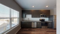 Located at 1010 Enclave Blvd in Edwardsville, Illinois, this contemporary single-floor residence offers a thoughtfully designed layout with modern finishes throughout. The kitchen serves as a standout feature, showcasing dark espresso-toned cabinetry with sleek hardware, light granite countertops, and a classic white subway tile backsplash. A full suite of stainless steel appliances — including a refrigerator, electric range, over-the-range microwave, and dishwasher — delivers both style and functionality. A large window floods the kitchen and open living area with natural light, creating a bright and welcoming atmosphere. Rich, dark hardwood-style flooring extends seamlessly throughout the unit, providing a warm and cohesive aesthetic. The bedroom is a well-proportioned space outfitted with a ceiling fan, a closet, and the same durable flooring, offering a comfortable and practical retreat. The bathroom features a full tub and shower combination with clean, neutral finishes that maintain the unit's modern sensibility. Recessed lighting and neutral gray wall tones contribute to the clean, contemporary character of the home, making it a polished and move-in ready space in the heart of Edwardsville.