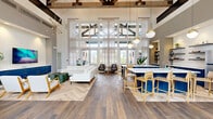 Located at 1430 Bell Rd in Nashville, TN, this impressive single-floor amenity space spans a generous footprint and is divided into two distinct yet equally compelling areas. The clubroom lounge and kitchen area showcases soaring double-height ceilings supported by exposed wood beam trusses, flooding the space with natural light through expansive floor-to-ceiling windows draped in sheer curtains. The open-concept layout features a herringbone-patterned hardwood floor that elegantly transitions throughout. A fully equipped kitchen island anchors the space, finished in bold navy cabinetry topped with white quartz countertops and surrounded by natural wood barstools. Pendant globe lights in brushed gold add warmth overhead. The lounge area offers plush white sofas, mid-century accent chairs, a wall-mounted flat-screen TV atop a coordinating navy credenza, and a striking sputnik chandelier. The second area houses a full indoor basketball court with a polished hardwood floor, regulation hoops, padded wall panels for safety, and a dramatic athlete mural as a focal point. Soaring ceilings and large clerestory windows bathe the court in natural light, creating an energetic and functional athletic environment.