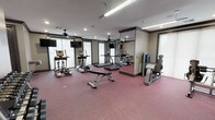 The Gentry's fitness center is a thoughtfully designed workout facility that provides residents with a comprehensive range of exercise options. The space features durable, cushioned flooring in a deep red tone throughout, providing a comfortable and functional surface for all types of exercise. Ceiling fans are mounted overhead alongside recessed lighting and fluorescent fixtures, ensuring the room remains well-lit and well-ventilated during workouts.

The cardio zone is well-appointed with multiple treadmills, elliptical trainers, and a stair-climbing machine, each positioned in front of wall-mounted flat-screen televisions for an engaging workout experience. Large windows with frosted roller shades line the perimeter, allowing natural light to filter in while maintaining privacy.

Full-length mirrors are strategically placed along the walls, visually expanding the space and allowing users to monitor their form. The strength training area features a well-stocked dumbbell rack with a wide range of free weights, a weight bench, and an adjustable resistance machine. A dedicated functional training zone includes a TRX suspension training system, wall-mounted medicine balls, and instructional workout guides. A water fountain is also conveniently available within the space, rounding out this fully equipped fitness facility.