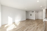 This single-floor unit presents a clean, contemporary design defined by an open-concept layout and consistent light wood-tone flooring throughout. Recessed lighting and crisp white walls create a bright, airy atmosphere across all areas of the space.

The kitchen is a standout feature, outfitted with a full suite of stainless steel appliances including a refrigerator, electric range, microwave, and dishwasher. Wood-grain cabinetry extends from counter height to the ceiling, providing generous storage, while the white countertops and tile backsplash add a modern contrast. The kitchen opens directly into the living area, supporting a seamless flow for daily living and entertaining.

The living space is generously proportioned, with large windows and a glass door leading to a private balcony that brings in natural light and outdoor views of the surrounding neighborhood. An additional room offers flexible use as a bedroom or secondary living area, featuring a window and direct balcony access.

The bathroom includes a full soaking tub with a curved shower curtain rod, toilet, and continues the light wood flooring found throughout the unit. A dedicated in-unit laundry area with stacked washer and dryer adds practical convenience. The electrical panel is accessible within the unit.