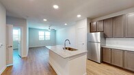 This well-designed single-floor unit offers a clean, contemporary aesthetic with an open-concept layout that seamlessly connects the kitchen and living area. The kitchen serves as the centerpiece, anchored by a central island with a granite countertop and an integrated sink. Rich, dark-toned shaker-style cabinetry lines the walls, complemented by a full suite of stainless steel appliances including a refrigerator, range, microwave, and dishwasher. Light hardwood-style flooring extends throughout the entire unit, creating a cohesive and warm atmosphere.

The living area is generously sized, illuminated by natural light from large windows and equipped with a ceiling fan. Recessed lighting throughout ensures bright, even illumination across all spaces. A dedicated in-unit laundry area with a washer and dryer provides added convenience.

The bedroom is a comfortable, well-lit retreat featuring a ceiling fan, a large window, and direct access to a bathroom. The bathroom features a granite-topped vanity with dark cabinetry, consistent with the kitchen's design language. A spacious walk-in closet with wire shelving on three walls offers ample organized storage. The unit's neutral color palette and modern finishes create a bright, move-in-ready living environment.