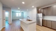 This well-designed single-floor unit offers a clean, contemporary aesthetic with an open-concept layout that seamlessly connects the kitchen and living area. The kitchen serves as the centerpiece, anchored by a central island with a granite countertop and an integrated sink. Rich, dark-toned shaker-style cabinetry lines the walls, complemented by a full suite of stainless steel appliances including a refrigerator, range, microwave, and dishwasher. Light hardwood-style flooring extends throughout the entire unit, creating a cohesive and warm atmosphere.

The living area is generously sized, illuminated by natural light from large windows and equipped with a ceiling fan. Recessed lighting throughout ensures bright, even illumination across all spaces. A dedicated in-unit laundry area with a washer and dryer provides added convenience.

The bedroom is a comfortable, well-lit retreat featuring a ceiling fan, a large window, and direct access to a bathroom. The bathroom features a granite-topped vanity with dark cabinetry, consistent with the kitchen's design language. A spacious walk-in closet with wire shelving on three walls offers ample organized storage. The unit's neutral color palette and modern finishes create a bright, move-in-ready living environment.