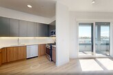 This thoughtfully designed two-story residence in Bayonne, NJ offers a bright, modern living experience across two well-proportioned floors. Light hardwood flooring flows throughout, complementing the clean white walls and recessed lighting that give every room an airy, contemporary feel.

The lower level features an open-concept kitchen and living area flooded with natural light through expansive floor-to-ceiling sliding glass doors that lead directly to a private balcony with open views of the surrounding neighborhood. The kitchen is outfitted with two-tone cabinetry—warm wood lower cabinets paired with sleek matte upper cabinets—and a full suite of stainless steel appliances, including a gas range, dishwasher, microwave, and refrigerator, all set against crisp white countertops.

The upper floor houses two well-sized bedrooms, each featuring large windows with sweeping outdoor views and generous closet space. The two bathrooms offer distinct, stylish finishes: one showcases dramatic marble-effect wall tile with a floating vanity and a backlit round mirror, while the other features a soaking tub surrounded by glossy gray subway tile. A dedicated laundry area and multiple closets throughout add practical convenience to this polished, move-in-ready home.