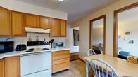 This two-floor residential space offers a practical and comfortable layout designed for everyday living. The kitchen is well-equipped with warm oak cabinetry, white appliances including a range, dishwasher, and refrigerator, along with ample counter space and tile flooring. A dedicated dining area adjacent to the kitchen provides space for casual meals. The living room features plush carpeting, a large window that allows natural light to filter in, and access to adjoining rooms through wood-trimmed doorways, creating a cohesive flow throughout the main level. The bedrooms are carpeted and generously sized, each with windows offering views of surrounding greenery. The full bathroom includes a single vanity with a large mirror, a tub-shower combination, and a clean, functional layout. A notable convenience is the in-unit laundry closet, which houses a stacked washer and dryer. Throughout the space, textured ceilings, neutral wall tones, and consistent warm wood trim provide a unified aesthetic. The overall layout is straightforward and efficiently organized, making it a functional and livable multi-floor residence.