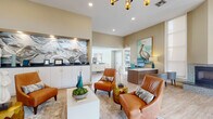 Located at 4200 Community Dr in West Palm Beach, FL, this single-floor leasing office for Azalea Village Apartments offers a welcoming and well-appointed environment designed with a modern coastal aesthetic. The open-concept layout is anchored by soaring ceilings that lend an airy, expansive feel to the entire space. Light-toned hardwood-style flooring runs throughout, complementing the warm neutral wall tones and crisp white trim.

The main reception area features a sleek workstation desk with seating for staff, positioned near large double entry doors that flood the space with natural light and provide views of the outdoor pool area. A statement mosaic-tiled fireplace adds a refined architectural focal point alongside tall transom windows. A stylish sputnik chandelier and recessed lighting illuminate the space throughout the day and evening.

The central lounge area is furnished with rich cognac leather armchairs, a white rectangular coffee table, and layered area rugs, creating an inviting space for prospective residents. A built-in credenza with a dramatic, backlit marble-effect art installation serves as a striking design centerpiece. Coastal-themed artwork, including ocean landscapes and a pelican portrait, reinforces the Florida-inspired character. Additional private offices branch off the main area, offering dedicated spaces for leasing consultations.