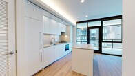 Located at 1280 Union St NE in Washington, DC, this modern one-bedroom, one-bathroom residence offers a thoughtfully designed single-level layout that maximizes every square foot. The open-concept kitchen is a standout feature, showcasing floor-to-ceiling white cabinetry, a stainless steel gas cooktop, built-in oven, and an integrated sink. A sleek center island with a neutral countertop provides additional workspace and casual dining. Large floor-to-ceiling glass doors and windows flood the kitchen and living area with natural light and offer views of the surrounding neighborhood. Light-toned hardwood flooring runs throughout, adding warmth to the crisp, contemporary aesthetic. The bedroom is a clean, minimalist space with light wood floors, white walls, and a mirrored sliding door that enhances the sense of space. An adjacent walk-in closet features built-in shelving and hanging rods for efficient storage. The bathroom is finished with large-format gray tile flooring, a floating white vanity with integrated storage, a backlit mirror cabinet, and a glass-enclosed walk-in shower with coordinating tile surround. The overall ambiance is bright, clean, and modern throughout.