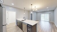 Located at 5510 Southwestern Blvd in Hamburg, NY, this well-designed 2-bedroom, 2-bathroom single-floor residence offers a clean, contemporary aesthetic with thoughtful finishes throughout. The open-concept layout seamlessly connects the kitchen, dining, and living areas, creating an inviting and functional shared space. The kitchen is a standout feature, anchored by a large center island with a white quartz countertop, dark cabinetry, a black matte faucet with undermount sink, and stainless steel appliances including a refrigerator, gas range, and microwave. Pendant lighting and a chandelier add character overhead, while light wood-look flooring ties the space together. The living area benefits from natural light through sliding glass doors that open to an exterior view. Both bedrooms are carpeted and feature ceiling fans; the primary bedroom is generously sized with two windows, while the secondary bedroom offers a comfortable, quiet retreat. The two bathrooms continue the modern theme with wood-look tile flooring and dark hardware accents. A dedicated in-unit laundry room with a full-size washer and dryer adds everyday convenience. Two closets and a hallway complete the efficient and well-organized floor plan.