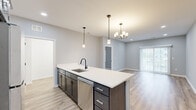 Located at 5510 Southwestern Blvd in Hamburg, NY, this well-designed 2-bedroom, 2-bathroom single-floor residence offers a clean, contemporary aesthetic with thoughtful finishes throughout. The open-concept layout seamlessly connects the kitchen, dining, and living areas, creating an inviting and functional shared space. The kitchen is a standout feature, anchored by a large center island with a white quartz countertop, dark cabinetry, a black matte faucet with undermount sink, and stainless steel appliances including a refrigerator, gas range, and microwave. Pendant lighting and a chandelier add character overhead, while light wood-look flooring ties the space together. The living area benefits from natural light through sliding glass doors that open to an exterior view. Both bedrooms are carpeted and feature ceiling fans; the primary bedroom is generously sized with two windows, while the secondary bedroom offers a comfortable, quiet retreat. The two bathrooms continue the modern theme with wood-look tile flooring and dark hardware accents. A dedicated in-unit laundry room with a full-size washer and dryer adds everyday convenience. Two closets and a hallway complete the efficient and well-organized floor plan.