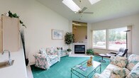 Located at 8424 N Nevada St in Spokane, Washington, this single-floor home offers a well-organized layout with a variety of functional and comfortable living spaces. The living room is a standout feature, boasting soaring vaulted ceilings, dual skylights that flood the space with natural light, and a ceiling fan. A tile-surround fireplace serves as a central focal point, while large windows frame views of the surrounding tree-lined neighborhood. Teal carpeting runs throughout the main living areas, lending a cohesive, warm feel to the home.

The kitchen is efficiently designed with light wood cabinetry, white appliances including a dishwasher and range, ample counter space, and windows that invite natural light and garden views. An adjacent dining area features vaulted ceilings and is illuminated by an elegant chandelier, with a built-in hutch adding storage and character.

The primary bedroom is generously sized with teal carpet, a sliding glass door opening to an outdoor deck, and an en-suite vanity area with access to a private bathroom. A secondary bedroom offers comfortable proportions with its own bathroom access. The bathrooms feature classic tile flooring with a diamond pattern and built-in cabinetry. Throughout the home, a consistent neutral palette with teal accents creates a light and airy ambiance.