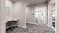 Located at 12612 Clermont Cir in Fort Worth, TX, this compact yet well-appointed professional workspace is thoughtfully designed to support both collaborative meetings and individual productivity. The space is organized across a single floor and comprises three distinct areas connected by a clean, open corridor.

The centerpiece is a dedicated conference room featuring a substantial walnut-finished rectangular table surrounded by upholstered rolling chairs. A wall-mounted flat-screen display provides presentation capabilities, while natural light filters in through windows dressed with white blinds. An eye-catching geometric linear chandelier anchors the ceiling, adding a refined aesthetic touch. Decorative wall art and circular wall accents contribute to the room's polished, professional character.

The corridor connecting the rooms is finished with neutral gray walls, white trim, and patterned loop-pile carpet that runs throughout the entire space, lending visual cohesion. Glass-paneled French doors provide transparency between areas while maintaining acoustic separation.

Adjacent to the main entry, a semi-private workstation area features built-in desk surfaces and individual seating — well-suited for focused, heads-down work. The entry area also includes a built-in marble-topped counter for additional workspace or reception use. Security access control is visible at the main entry door, which features a bold navy blue finish that adds a distinctive design accent to the space.