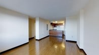 Located at 300 Tresser Blvd in downtown Stamford, Connecticut, this two-bedroom, one-bathroom residence offers a well-designed single-floor layout that maximizes comfort and functionality. The open-concept living and dining area is anchored by warm hardwood flooring that runs throughout, lending a clean and cohesive aesthetic to the space. Smooth white walls and flush ceiling lighting create a bright, neutral backdrop that lends itself to a variety of interior styles. The kitchen is positioned at the heart of the home, featuring a peninsula with rich wood-paneled cabinetry that provides both workspace and subtle visual separation between the kitchen and living area. Upper and lower cabinetry in a deep walnut tone offer generous storage, while the white appliances contribute a clean, classic finish. A structural column and partial wall create a natural entry zone, adding architectural definition without disrupting the open feel of the main living space. Two bedrooms provide comfortable private retreats, while the balcony extends the living space outdoors, offering a pleasant spot to enjoy the surrounding Stamford skyline and urban environment. This residence combines practical layout design with warm finishes in a prime downtown location.