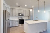 Located at 138 Rosewick Corner Pl in La Plata, MD, this well-designed one-bedroom, one-bathroom residence offers a thoughtfully organized single-floor layout with a clean, contemporary aesthetic throughout. Light-toned hardwood-style flooring flows seamlessly across the entire space, complementing the bright, neutral color palette on the walls and ceilings.

The open-concept kitchen, dining, and living area serves as the heart of the home. The kitchen is appointed with gray shaker-style cabinetry, a white subway tile backsplash, stainless steel appliances including a refrigerator, electric range, and over-the-range microwave, and a central island with a white countertop, undermount sink, and pendant lighting above. Recessed ceiling lights provide additional illumination throughout the shared living space.

The bedroom is a well-proportioned, quiet retreat featuring a ceiling fan, a large window that brings in abundant natural light and outdoor views, and access to two closets for ample storage.

The full bathroom is finished with a wide dual-sink vanity featuring gray shaker cabinetry, a white countertop, a large mirror, and subway tile detailing in the shower area. A dedicated in-unit laundry room with wire shelving and washer/dryer hookups adds everyday convenience to this move-in-ready residence.