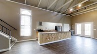 Located at 4334 Appian Way W in Gahanna, Ohio, this single-floor space offers an open and versatile layout well-suited for a variety of uses. The interior immediately impresses with its soaring vaulted ceiling accented by exposed white-painted beams, lending the space a rustic yet refined architectural character.

The open main area is anchored by a generous kitchen equipped with stainless steel appliances, including a refrigerator and a gas range with a wall-mounted ventilation hood. Rich wood cabinetry lines the kitchen walls, complemented by granite-style countertops that add a layer of durability and style. A standout feature is the large, elongated kitchen island clad in natural wood paneling with a matching countertop surface, providing ample workspace and a natural gathering point.

Wide-plank hardwood-style flooring runs throughout, adding warmth and cohesion to the open floor plan. Natural light streams in through a tall arched window dressed with vertical blinds, brightening the space and enhancing its airy feel. The neutral, warm-toned walls throughout create a welcoming and adaptable environment. The thoughtful combination of functional design elements and architectural detail makes this a highly practical and visually appealing space.