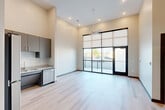 Located at 900 E Main St in Chattanooga, TN, this modern one-bedroom, one-bathroom unit offers a thoughtfully designed layout with contemporary finishes throughout. The open-concept living and kitchen area immediately impresses with soaring ceilings and a dramatic floor-to-ceiling glass wall with black-framed doors that open to a private balcony, flooding the space with natural light. A ceiling fan complements the airy atmosphere of the living area, which is finished with light-toned hardwood-style flooring that extends throughout the unit.

The kitchen is well-appointed with grey flat-front cabinetry, granite countertops, and a full suite of stainless steel appliances, including a refrigerator, electric range, dishwasher, and built-in microwave. Ample upper and lower cabinet storage makes the kitchen both functional and stylish.

The bedroom offers a comfortable footprint with a tall window bringing in natural light, and direct access to a spacious walk-in closet outfitted with wire shelving and hanging rods. The bathroom features granite countertops on a floating vanity, a large wall mirror, and a full soaking tub with a handheld shower. An in-unit laundry area rounds out the practical amenities of this clean, modern residence.