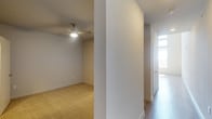 This two-story residence offers two bedrooms and two bathrooms thoughtfully arranged across its floors. The interior features a clean, neutral aesthetic with smooth walls finished in soft, warm tones throughout. Carpeted bedroom areas provide a comfortable underfoot feel, while hard surface flooring is present in the hallway and transitional spaces, creating a practical distinction between living zones. A ceiling fan is installed in one of the bedrooms, contributing both comfort and airflow to the space. The hallway connects the rooms efficiently, with a closeted storage area featuring double doors visible along the corridor. Natural light filters into the space through a window at the end of the hall, brightening the passage between rooms. The overall design is straightforward and well-maintained, with consistent baseboards and trim detailing throughout. The two-floor layout offers a sense of separation between living and sleeping areas, making the home adaptable for a variety of lifestyles. The neutral finishes and practical flooring choices create a versatile backdrop suitable for a range of furnishing styles.