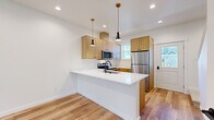 Located in Bellingham, WA, this thoughtfully designed two-story home offers 2 bedrooms and 3 bathrooms across two well-proportioned floors. The main level features an open-concept kitchen and living area bathed in natural light. The kitchen is a standout, showcasing warm wood cabinetry, a crisp white waterfall island with an undermount sink, stainless steel appliances, and stylish black pendant lighting — all set atop light-toned hardwood flooring that flows seamlessly throughout the main level. A half bathroom on the main floor features a matching wood vanity with white countertop, consistent with the home's modern aesthetic. The staircase connects to the upper floor, where both bedrooms are found. The primary bedroom offers a generous footprint with plush carpeting, a walk-in closet, and a private en-suite bathroom. The second bedroom is bright and airy, with a large window framing neighborhood views and the same warm hardwood flooring as seen downstairs. A well-appointed full bathroom with a soaking tub and matte black fixtures serves the upper level. Throughout, crisp white walls, clean lines, and a cohesive palette of natural wood tones create a modern yet inviting atmosphere.