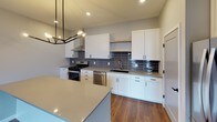 This single-floor space combines modern design with practical functionality across a thoughtfully arranged layout. The open living area is anchored by rich hardwood-style flooring and features soaring ceilings with exposed ductwork, lending an industrial-modern character to the space. Large windows fill the living and bedroom areas with natural light while offering views of the surrounding urban skyline.

The kitchen is a standout feature, equipped with crisp white shaker cabinetry, quartz countertops, and a striking gray subway tile backsplash. Stainless steel appliances — including a gas range, dishwasher, and refrigerator — complete the space, which also includes a central island for additional prep and gathering space. Matte black hardware throughout the kitchen adds a refined, contemporary touch.

Two bathrooms serve the unit: one features a glass-enclosed walk-in shower and black accent fixtures, while the second includes a full soaking tub and shower combination with a white vanity and matching black hardware. Both bathrooms are finished with hardwood-style flooring consistent with the rest of the unit.

A dedicated laundry room houses a full-size Whirlpool front-load washer and dryer, complemented by built-in shelving for storage. Hallways are clean and well-proportioned, with neutral gray walls and white trim creating a cohesive, modern aesthetic throughout.