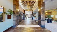 Located at 3310 S Kenton St in Denver, CO, this beautifully appointed single-floor clubhouse offers a refined and welcoming community space. The grand entrance corridor sets the tone immediately, featuring rich stone tile flooring, bold wood-clad columns, and a striking slatted ceiling detail with warm pendant lighting that draws the eye inward toward the light-filled interior beyond.

The main lounge area exudes sophistication, with soft blue-gray walls, large framed frosted-glass panels, and floor-to-ceiling windows that flood the space with natural light and offer views to the outdoors. Elegant seating arrangements, mixed-material coffee tables, and curated artwork create an inviting, upscale atmosphere.

The kitchen and bar area is a standout feature, centered around a curved, multi-tiered bar finished in rich wood and gold metalwork, encircled by upholstered bar stools. Deep mahogany cabinetry, stainless steel appliances, and a clean white countertop complete the well-equipped kitchen. A cluster of sculptural gold pendant lights adds dramatic visual interest overhead.

A dedicated office space with plush carpet, multiple windows, and ample natural light provides a quiet, functional area for focused work. Throughout the clubhouse, lush indoor plants, contemporary artwork, and a cohesive warm-toned palette unify the space into a polished, community-centered environment.