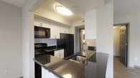 Located at 1480 Runaway Bay Dr in Columbus, Ohio, this single-floor unit offers a thoughtfully designed layout with modern finishes throughout. The kitchen is a standout feature, equipped with black appliances including a range, microwave, and refrigerator, complemented by white cabinetry with sleek hardware, a subway tile backsplash, and dark granite countertops that extend to a peninsula with an undermount stainless steel sink — ideal for both cooking and casual dining. The open-concept design allows the kitchen to flow seamlessly into the dining and living areas, which are finished with durable wood-look vinyl flooring. The living room benefits from a large sliding glass door that fills the space with natural light and provides outdoor views. The bedroom features plush carpeting and a window with a view of the surrounding greenery, creating a comfortable retreat. A generously sized walk-in closet with built-in shelving and hanging rods provides ample storage. The full bathroom is finished with wood-look flooring, a white vanity with dark granite countertops, a large mirror, and a full tub-shower combination. Completing the unit is a dedicated in-unit laundry space housing a full-size washer and dryer.