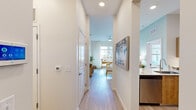 This thoughtfully designed single-floor residence offers three bedrooms and three bathrooms within a compact yet efficiently organized floor plan. Light wood-tone flooring runs throughout the main living areas and hallways, contributing to a clean, cohesive aesthetic. The entryway hallway leads seamlessly toward the open living room, which features soaring ceilings, a ceiling fan, and large windows dressed with sheer white curtains that invite abundant natural light. A soft sage-green accent wall paired with curated wall art lends the living space a relaxed, coastal character.

The kitchen is equipped with warm wood cabinetry, stainless steel appliances including a refrigerator, range, and microwave, complemented by a tiled backsplash and a generous white quartz peninsula with bar seating — ideal for casual dining or entertaining.

Each of the three bedrooms offers natural light through well-sized windows with views of the outdoor surroundings, and carpeted flooring for added comfort. The primary bedroom includes a walk-in closet with built-in shelving. The bathrooms feature wood-toned vanities and hard surface flooring, with one bathroom showcasing distinctive woven wall décor that adds a bohemian touch. Throughout, the space maintains a bright, neutral palette that creates a welcoming and versatile living environment.