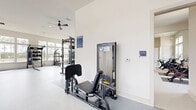 Located in Santa Rosa Beach, FL, this single-floor fitness facility offers a comprehensive workout environment across two dedicated exercise rooms. The main gym area is generously sized, featuring soaring ceilings and an expansive bank of large windows that flood the space with natural light and provide scenic outdoor views, including glimpses of a pool and surrounding landscape. The durable speckled flooring throughout is well-suited for high-traffic fitness use.

The main exercise room is outfitted with a wide array of equipment, including a TRX suspension training station, a power rack with weight plates, selectorized cable machines, a leg press machine, a multi-rack dumbbell station, an adjustable workout bench, and full-length wall mirrors that enhance the sense of space. Ceiling fans circulate air throughout the open layout, while a wall-mounted TV adds a media element for entertainment during workouts.

A dedicated cardio area includes treadmills, an elliptical, and rowing machines, all positioned against large windows overlooking the outdoors. An adjoining yoga room provides a quieter, more focused space, while a separate room houses Peloton-style cycling bikes with individual screens. Together, these spaces deliver a thorough and well-appointed fitness experience.