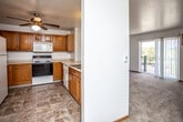 This single-floor unit is organized around a practical, open-concept layout that connects the kitchen and living areas seamlessly. The kitchen is equipped with warm oak cabinetry extending to the upper walls, a white electric range, microwave, refrigerator, and a double sink set into a peninsula counter. Tile flooring in a stone-like pattern runs throughout the kitchen, providing a durable and easy-to-maintain surface. A ceiling fan overhead adds air circulation to the space.

The living area flows directly from the kitchen and features neutral carpet, white walls, and a sliding glass door that opens to a private balcony, allowing natural light and outdoor views into the room. A wall-mounted air conditioning unit serves the living space. The bedroom is carpeted and comfortably sized, with a ceiling fan, a wall A/C unit, a baseboard heater, and a window offering natural light and exterior views.

The bathroom includes tile flooring, a full tub and shower combination with a chrome curtain rod, a toilet, and a wood-toned vanity. Throughout the unit, clean white walls and consistent finishes contribute to a straightforward, functional ambiance.