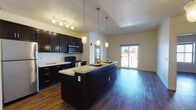 Located at 500 S Mesa Hills Drive in El Paso, Texas, this single-floor residence offers a well-designed layout with cohesive finishes throughout. The kitchen serves as a centerpiece of the living area, featuring dark espresso cabinetry, light countertops, stainless steel appliances including a refrigerator and microwave, and a black range. A generous kitchen island with an integrated sink provides additional prep space and seating, illuminated by stylish pendant lights that hang from notably elevated ceilings. The open-concept design allows the kitchen to flow naturally into the living area, which is bathed in natural light from a sliding glass door that opens to a private balcony with outdoor views of the surrounding El Paso landscape and distant mountains. Rich hardwood-style flooring runs consistently throughout the unit, lending warmth and continuity. The bedrooms are well-proportioned, with ceiling fans, natural light, and access to hallways connecting to the bathrooms. The bathroom features tile-surround tub and shower combination, dark vanity cabinetry, and light countertops. A dedicated laundry room with full-size washer and dryer hookups and built-in shelving adds practical convenience to the layout.