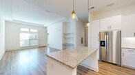 Located at 4271 Woodward Mill Rd in Buford, GA, this two-story home offers a well-designed layout that blends modern finishes with functional living spaces. The main level showcases an open-concept kitchen and living area, anchored by a large granite-topped island with elegant pendant lighting overhead. White shaker cabinetry, a decorative tile backsplash, and a full suite of stainless steel appliances—including a refrigerator with ice maker, range, microwave, and dishwasher—complete the kitchen. The living area flows naturally from the kitchen and features light wood-look flooring, a built-in shelving niche, and generous natural light from front-facing windows. Carpeted stairs with a white handrail lead to the upper level, where the bedrooms continue the home's clean, neutral aesthetic. One bedroom features transom-style windows that draw in abundant natural light and light wood flooring. A walk-in closet with wire shelving provides ample storage. The upper-level hallway connects to a bathroom showcasing granite countertops and large-format tile. On the lower level, a spacious attached two-car garage with concrete flooring and an automatic opener provides convenient access. An additional utility room with concrete flooring offers extra storage potential. Throughout, crisp white walls and consistent finishes create a bright, cohesive atmosphere.