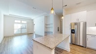 Located at 4271 Woodward Mill Rd in Buford, GA, this two-story home offers a well-designed layout that blends modern finishes with functional living spaces. The main level showcases an open-concept kitchen and living area, anchored by a large granite-topped island with elegant pendant lighting overhead. White shaker cabinetry, a decorative tile backsplash, and a full suite of stainless steel appliances—including a refrigerator with ice maker, range, microwave, and dishwasher—complete the kitchen. The living area flows naturally from the kitchen and features light wood-look flooring, a built-in shelving niche, and generous natural light from front-facing windows. Carpeted stairs with a white handrail lead to the upper level, where the bedrooms continue the home's clean, neutral aesthetic. One bedroom features transom-style windows that draw in abundant natural light and light wood flooring. A walk-in closet with wire shelving provides ample storage. The upper-level hallway connects to a bathroom showcasing granite countertops and large-format tile. On the lower level, a spacious attached two-car garage with concrete flooring and an automatic opener provides convenient access. An additional utility room with concrete flooring offers extra storage potential. Throughout, crisp white walls and consistent finishes create a bright, cohesive atmosphere.