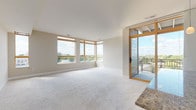 This thoughtfully designed single-floor space offers a seamless blend of modern finishes and comfortable living. The expansive main living area is bathed in natural light from a bank of large, wood-framed corner windows, complemented by plush wall-to-wall carpeting and neutral-toned walls that create a clean, inviting atmosphere. A wood-framed glass door opens directly onto a private balcony, extending the living space outdoors with panoramic views of the surrounding treetops and cityscape.

The kitchen is a standout feature, showcasing rich dark wood cabinetry, granite countertops, a breakfast bar peninsula, and a full suite of stainless steel appliances including a range, over-the-range microwave, and French door refrigerator. Light hardwood-style flooring anchors the kitchen and dining area, contrasting elegantly with the cabinetry.

The bedrooms are generously proportioned, each finished with soft carpeting and large windows that frame bright outdoor views. Two well-appointed bathrooms feature dark wood vanities, white countertops, large mirrors, and tile flooring — one with a walk-in shower and the other with a tub/shower combination. Additional highlights include a spacious walk-in closet with built-in wire shelving, providing ample organized storage throughout the unit.