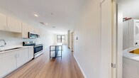 This thoughtfully designed 1-bedroom, 2-bathroom unit offers a contemporary living experience across a single floor. The open-concept layout connects the kitchen and living areas, creating a seamless, airy flow. The kitchen is a standout feature, outfitted with white shaker cabinetry reaching to the ceiling, a full suite of stainless steel appliances including a refrigerator, electric range, microwave, and dishwasher, and a light-toned countertop with a clean tile backsplash. A freestanding kitchen island with a matte stone surface and open lower shelving adds both prep space and visual interest.

Wood-tone plank flooring runs throughout the unit, complementing the bright white walls and adding warmth to the modern aesthetic. Recessed lighting provides consistent illumination across the main living areas. The bedroom is well-proportioned, featuring a large black-framed window that invites generous natural light and offers outdoor views of the surrounding neighborhood. A walk-in closet with wire shelving provides practical storage. Both bathrooms are finished in a clean, minimalist style with wood-tone flooring, white vanities, and a full tub-shower combination. A dedicated laundry area completes this well-appointed unit.
