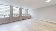 This thoughtfully designed 1-bedroom, 1-bathroom residence offers a bright, modern living experience across a single floor. Light-toned hardwood flooring runs consistently throughout the unit, lending a cohesive and airy feel to every room.

The spacious living room is a standout feature, boasting a wall of large windows that frame sweeping urban views, flooding the space with natural light. The open layout provides ample room for flexible furniture arrangements.

The kitchen is well-equipped with stainless steel appliances, including a full-size refrigerator and a range, complemented by sleek white cabinetry and clean countertops. Recessed lighting ensures the workspace is well-lit and functional.

A hallway system connects the main living areas to the private quarters, providing clear separation and circulation. The bedroom offers a comfortable footprint with a built-in double-door closet for generous storage. Neutral gray-toned walls create a calm, restful atmosphere.

The bathroom features a clean white finish with marble-accented shower walls, light tile flooring, and a streamlined vanity. The overall design of the unit emphasizes a minimalist, contemporary aesthetic with neutral tones, clean lines, and modern finishes throughout.