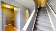 Located at 300 Executive Dr in Newark, Ohio, this two-story residence offers a practical and well-organized layout across two levels. The main floor features a kitchen equipped with gray cabinetry, granite-style countertops, a double-basin sink, and white appliances including an electric range and refrigerator. Hardwood-style flooring runs through the kitchen area, complementing the neutral gray walls found throughout the home. A main-floor bathroom is conveniently accessible from the central hallway. A carpeted staircase with white railings connects the two levels, leading to the upper floor. The living areas feature plush gray carpeting and neutral gray wall tones, creating a cohesive and understated aesthetic. Bedrooms on the upper level include closet space with built-in hanging rods for storage. One room features a sliding glass door fitted with vertical blinds, offering views of the surrounding outdoor greenery and bringing in natural light. Additional rooms upstairs provide flexible space, each carpeted and move-in ready. Textured ceilings are present throughout, and the overall design emphasizes clean lines and a neutral palette, making the space adaptable for a variety of living arrangements.