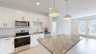 Located at 1 Hatcher Drive in Stockbridge, GA, this well-designed 2-bedroom, 3-bathroom single-story home offers a clean, modern aesthetic throughout. Light wood flooring runs continuously across the space, creating a cohesive and bright atmosphere.

The kitchen serves as a standout feature, outfitted with crisp white shaker cabinetry accented by matte black hardware, granite countertops, and a herringbone tile backsplash. A spacious island with matching granite provides additional prep and seating space. Stainless steel appliances — including a French door refrigerator with ice dispenser, electric range, over-the-range microwave, and dishwasher — complete the well-equipped kitchen. Pendant lighting adds a polished finishing touch.

Both bedrooms are bright and airy, each featuring ceiling fans, large windows with blinds, and white panel doors with sleek black hardware. The primary bedroom includes a generously sized walk-in closet with floor-to-ceiling wire shelving for ample organized storage. A second walk-in closet offers equally practical storage solutions.

The bathrooms maintain the home's modern design language, with granite-topped white vanities, large mirrors, and a tiled soaking tub with shower combination. The clean white tile surround adds a timeless, polished feel to the bath areas.