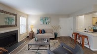 This single-floor residence offers a thoughtfully designed layout that balances comfort and functionality throughout its living spaces. The living room serves as the centerpiece of the home, featuring a wood-burning fireplace flanked by windows dressed with horizontal blinds that allow ample natural light to filter in. Wood-look flooring runs throughout the main living areas, adding warmth and cohesion to the space.

The dining area is positioned adjacent to the living room and benefits from a large sliding glass door that opens to an outdoor view, complemented by a stylish overhead pendant light. The kitchen is equipped with light wood cabinetry, granite-style countertops, and black appliances including a range and full-size refrigerator, all set on matching wood-look flooring.

The bedroom is generously sized, finished with plush carpeting, and features a sliding glass door providing additional outdoor access and natural light. It connects directly to a dedicated vanity area with granite-style countertops, a large mirror, and a walk-in closet. A full bathroom with a tub-shower combination and wood-look flooring serves the unit. A separate laundry room accommodates a full-size washer and dryer, adding everyday convenience.