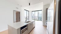 Located in the heart of Midtown Atlanta, this thoughtfully designed one-bedroom, one-bathroom residence offers a sleek, modern aesthetic throughout. Light hardwood flooring flows seamlessly across the open-concept layout, complemented by crisp white walls and abundant natural light. The combined kitchen and living area is a standout, anchored by a central island featuring a stainless steel sink, built-in microwave, and ample white quartz countertop space. Soft gray cabinetry with matte black hardware, a vertical tile backsplash, and integrated appliances complete the contemporary kitchen. Floor-to-ceiling windows frame breathtaking panoramic views of the Atlanta skyline and lush green canopy below, flooding the living space with natural light. The bedroom continues the light hardwood flooring and benefits from its own dramatic floor-to-ceiling window with striking city views. A dedicated walk-in closet offers customizable shelving and hanging storage. The bathroom features marble-look tile flooring, a dual-sink vanity with white countertops and matte black fixtures, a large mirror, and a glass-enclosed walk-in shower with white square tile surround. A hallway connects all spaces efficiently, completing this well-appointed urban residence.