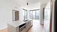 Located in the heart of Midtown Atlanta, this thoughtfully designed one-bedroom, one-bathroom residence offers a sleek, modern aesthetic throughout. Light hardwood flooring flows seamlessly across the open-concept layout, complemented by crisp white walls and abundant natural light. The combined kitchen and living area is a standout, anchored by a central island featuring a stainless steel sink, built-in microwave, and ample white quartz countertop space. Soft gray cabinetry with matte black hardware, a vertical tile backsplash, and integrated appliances complete the contemporary kitchen. Floor-to-ceiling windows frame breathtaking panoramic views of the Atlanta skyline and lush green canopy below, flooding the living space with natural light. The bedroom continues the light hardwood flooring and benefits from its own dramatic floor-to-ceiling window with striking city views. A dedicated walk-in closet offers customizable shelving and hanging storage. The bathroom features marble-look tile flooring, a dual-sink vanity with white countertops and matte black fixtures, a large mirror, and a glass-enclosed walk-in shower with white square tile surround. A hallway connects all spaces efficiently, completing this well-appointed urban residence.