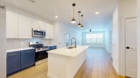 Located at 5815 S Elk Way in Aurora, CO, this well-appointed 2-bedroom, 2-bathroom residence offers a thoughtfully designed single-level layout with modern finishes throughout. The open-concept kitchen and living area serves as the heart of the home, anchored by a large central island with a white quartz countertop, a deep basin sink with a commercial-style pull-down faucet, and striking navy lower cabinetry contrasted by crisp white upper cabinets. A hexagonal tile backsplash and stainless steel appliances, including a gas range, microwave, and refrigerator, complete the kitchen. A trio of brass-accented pendant lights adds a contemporary touch overhead. Warm wood-look flooring extends seamlessly throughout the entire space, lending a cohesive and inviting feel. The living area is bright and open, benefiting from natural light through large windows and a ceiling fan for added comfort. Both bedrooms are generously proportioned, each featuring ceiling fans and dedicated closets with built-in shelving and hanging rods. The primary bathroom is elegantly finished with floor-to-ceiling tile, a backlit vanity mirror, dark cabinetry with gold hardware, and direct access to a walk-in closet. A dedicated laundry room with a full-size washer and dryer adds everyday convenience to this move-in-ready home.