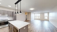 Located at 1850 Green Bay Rd in Highland Park, IL, this generously sized 5-bedroom, 3-bathroom residence offers an expansive, single-floor layout designed for comfortable living. The open-concept kitchen is a standout feature, boasting slate-gray shaker cabinetry with gold hardware, a large quartz-topped center island, a chevron-patterned tile backsplash, stainless steel appliances, and bold black pendant lighting overhead. Hardwood-style flooring flows throughout the main living areas, adding warmth and continuity to the space. The five bedrooms offer a mix of hardwood-style and plush carpeted flooring, with several rooms featuring multiple windows that invite ample natural light. The generously sized primary bedroom includes a well-appointed walk-in closet with built-in shelving, hanging rods, and dedicated storage sections. Three full bathrooms are finished with clean, modern tile work and frameless glass-enclosed walk-in showers with rain showerheads. One bathroom features an ADA-accessible shower with safety grab bars. The dedicated laundry room impresses with matching gray cabinetry, a quartz countertop, an under-counter sink, and in-unit washer. With four closets throughout, storage is plentiful. The overall aesthetic is clean, contemporary, and move-in ready.