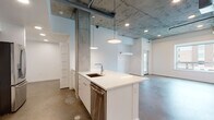 This single-floor unit showcases a striking industrial-modern aesthetic defined by exposed concrete ceilings with raw, textured finishes and polished concrete floors that run throughout the space. Structural concrete columns add an authentic loft character, while crisp white walls provide a clean contrast throughout.

The open-concept kitchen is a central highlight, featuring a large waterfall-edge island with an undermount sink, white lower cabinetry, and dark espresso upper cabinets. Stainless steel appliances — including a gas range, built-in microwave, and French door refrigerator — complete the kitchen's modern and functional design. Pendant lights hang above the island, complementing the recessed lighting overhead.

The living area flows seamlessly from the kitchen, benefiting from soaring ceiling heights that amplify the sense of openness. Bedrooms are generously proportioned with clean white walls and polished concrete floors; one bedroom features a large window offering views of the surrounding neighborhood and greenery, filling the room with natural light.

The bathrooms maintain the same clean, modern palette, featuring white cabinetry with chrome hardware, undermount sinks, and full tub-shower combinations clad in white subway tile. The polished concrete flooring continues here as well, reinforcing the unit's cohesive industrial character throughout every room.