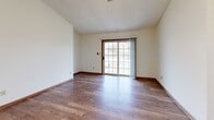 This single-floor, 2-bedroom, 2-bathroom unit in Fond du Lac, Wisconsin, offers a practical and comfortable layout with consistent finishes throughout. The galley-style kitchen is well-equipped with ample upper and lower cabinetry in a warm oak and cream combination, white appliances including a refrigerator, range, and dishwasher, a double-basin sink, and durable hardwood-style flooring — all topped by a textured ceiling with a skylight that adds natural brightness. The living room is a generous open space featuring the same hardwood-style flooring, a textured ceiling, and a large sliding glass door that fills the room with natural light and provides outdoor access. Both bedrooms are carpeted and feature natural light from windows, with warm wood-trimmed doors and trim throughout. The spacious primary bedroom benefits from a vaulted ceiling and walk-in closet with built-in wire shelving for ample storage. The two bathrooms are well-appointed: one features a tub/shower combination with a wide vanity and hardwood-style flooring, while the second includes a sliding glass-door shower enclosure. Warm wood trim and neutral tones tie the entire space together, creating a cohesive and functional living environment.