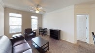 This single-floor unit offers a well-organized layout designed for comfortable everyday living. The living area is carpeted and finished with crown molding, featuring a ceiling fan with a light fixture and windows that allow natural light to fill the room. The space accommodates a seating arrangement alongside a small dining table and bookshelf, creating a versatile area for both relaxing and dining.

The kitchen is efficiently designed with white cabinetry, laminate countertops, and hardwood-style flooring. It includes a full suite of white appliances — a refrigerator, electric range, and over-the-range microwave — as well as a double-basin sink. Track lighting overhead provides ample illumination. A peninsula with a raised breakfast bar and bar seating connects the kitchen to the adjacent living space, enhancing the open feel and providing additional dining options.

The unit includes two bathrooms, each with a white vanity, single-basin sink, and warm-toned countertops. One bathroom features a combined tub and shower with tile surround and recessed lighting, while the second offers a similar setup with warm ambient lighting and built-in drawer storage. Both bathrooms are finished with tile flooring, offering a clean and functional aesthetic throughout.