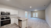 Located at 2308 Holiday Loop in Reidsville, NC, this single-story, one-bedroom, one-bathroom home offers a thoughtfully designed layout ideal for comfortable everyday living. The open-concept main area seamlessly combines the kitchen, dining, and living room into one cohesive space. The kitchen is outfitted with crisp white shaker-style cabinetry, granite-look countertops, a peninsula with a stainless steel sink, and a full suite of stainless steel appliances including a refrigerator, range, microwave, and dishwasher. Luxury vinyl plank flooring runs through the kitchen and entry areas, while plush carpeting extends across the living and bedroom spaces. The living room is bright and open, anchored by French doors that lead to a private patio and allow natural light to fill the room. The generously sized primary bedroom features soaring ceilings, a ceiling fan, and access to two closets, including a walk-in. The bathroom includes a walk-in shower with built-in shelving and a granite-top vanity. A dedicated laundry room with wire shelving and washer/dryer hookups adds everyday convenience. Neutral tones and recessed lighting throughout give the home a clean, modern aesthetic.