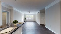 Located at 50 Creekside Dr in Kennesaw, GA, this single-floor residence offers a thoughtfully designed layout with a clean, neutral aesthetic throughout. The entryway welcomes visitors with elegant wainscoting panels, crown molding, and rich dark hardwood-style flooring that extends through the main living areas, setting a polished tone from the moment you step inside.

The open-concept living and dining area is generously proportioned, bathed in natural light from large windows that frame views of the surrounding greenery. Crown molding and a ceiling fan add refined detail overhead, while the open sightlines create a seamless flow between spaces.

The kitchen is outfitted with white cabinetry, dark stone-finish countertops, a classic subway tile backsplash, and stainless steel appliances including a range and over-the-range microwave. A breakfast bar connects the kitchen to the living area, making it ideal for casual dining and entertaining.

The bedroom features plush carpeting, a bright window with natural light, and access to a spacious walk-in closet equipped with wire shelving along multiple walls for generous storage. The bathroom includes a full tub and shower combination with white tile surround and hardwood-style flooring, completing this well-rounded residence.