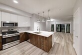 Located at 1721 Motor Parkway in Hauppauge, NY, this well-appointed one-bedroom, one-bathroom residence offers a thoughtfully designed open-concept layout with generous living space across a single floor. Light-toned hardwood-style flooring flows throughout the main living areas, lending a clean and cohesive aesthetic.

The kitchen is a standout feature, showcasing two-tone cabinetry — sleek white upper cabinets paired with rich walnut-finish lower cabinets — complemented by a white quartz waterfall island with an undermount sink and stylish pendant lighting. Stainless steel appliances, including a gas range, microwave, and refrigerator, complete this modern culinary space. The kitchen opens seamlessly into the living area, which is anchored by a ceiling fan and leads to a private balcony through full-height sliding glass doors.

The bedroom is a comfortable retreat, featuring plush carpeting and its own ceiling fan. It connects directly to a luxurious bathroom finished in striking marble-look tile from floor to ceiling, including a frameless glass walk-in shower and a wood-finish vanity with a white countertop. An organized walk-in closet with built-in shelving and chrome hardware provides excellent storage. The overall ambiance is modern, bright, and move-in ready.
