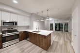 Located at 1721 Motor Parkway in Hauppauge, NY, this well-appointed one-bedroom, one-bathroom residence offers a thoughtfully designed open-concept layout with generous living space across a single floor. Light-toned hardwood-style flooring flows throughout the main living areas, lending a clean and cohesive aesthetic.

The kitchen is a standout feature, showcasing two-tone cabinetry — sleek white upper cabinets paired with rich walnut-finish lower cabinets — complemented by a white quartz waterfall island with an undermount sink and stylish pendant lighting. Stainless steel appliances, including a gas range, microwave, and refrigerator, complete this modern culinary space. The kitchen opens seamlessly into the living area, which is anchored by a ceiling fan and leads to a private balcony through full-height sliding glass doors.

The bedroom is a comfortable retreat, featuring plush carpeting and its own ceiling fan. It connects directly to a luxurious bathroom finished in striking marble-look tile from floor to ceiling, including a frameless glass walk-in shower and a wood-finish vanity with a white countertop. An organized walk-in closet with built-in shelving and chrome hardware provides excellent storage. The overall ambiance is modern, bright, and move-in ready.