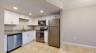 Located at 9700 Hamlin Blvd in Seminole, Florida, this single-floor, 2-bedroom, 2-bathroom residence offers a functional and well-appointed layout. The kitchen stands out with crisp white shaker cabinetry, granite-look countertops, recessed lighting, a textured ceiling, and a full suite of stainless steel appliances including a refrigerator, range, over-the-range microwave, and dishwasher. Light-toned ceramic tile flooring flows through the kitchen and living areas, contributing to a bright, clean aesthetic. The spacious living room features sliding glass doors with vertical blinds, providing access to an outdoor area and allowing natural light to fill the space. Both bedrooms are carpeted and feature neutral wall tones and windows with blinds. The primary bedroom is generously sized, offering dual closets with bifold doors for ample storage. The second bedroom also features a closet and a window with natural light. Each bathroom is finished with tile flooring, a white vanity, and a toilet. One bathroom includes a tub-shower combo, while the other features a standalone shower stall. A hallway connects the bedrooms and bathrooms, rounding out a practical and comfortable floor plan.